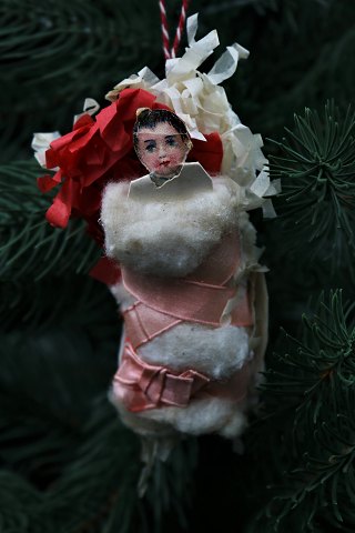 Gammelt juletræspynt i pap , silkepapir og vat i form af det lille svøbte jesusbarn. Længde: 10cm.